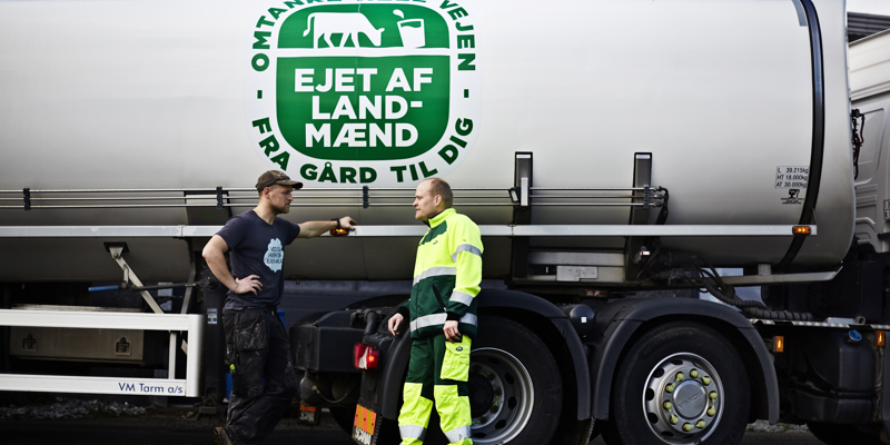 To mennesker taler foran en lastbil med en mælketank